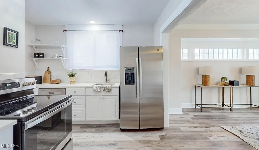 Kitchen with appliances with stainless steel finishes, white cabinets, durable wood-style vinyl floors, open shelves, and crown molding