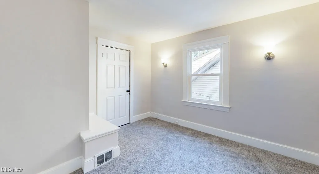 Back bedroom with wall sconces, light carpet and door to back balcony
