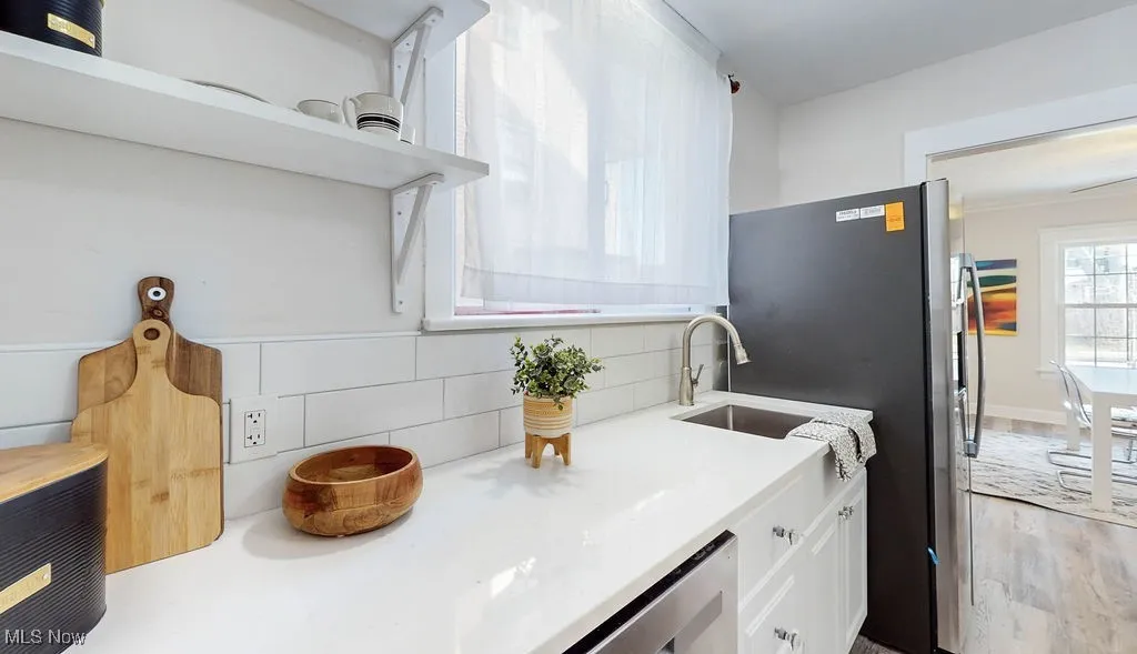 Kitchen with white cabinets, stainless steel fridge, light quartz stone counters, open shelves, and large bright window