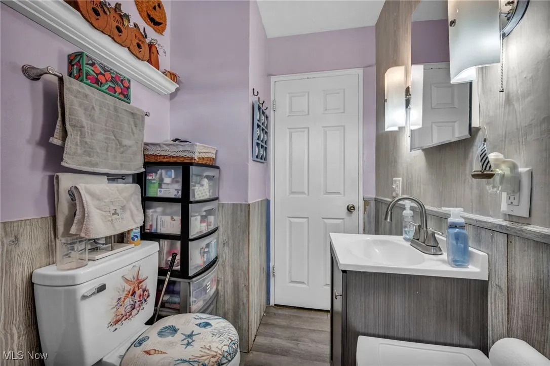 Half bathroom featuring a wainscoted wall, vanity, and dark wood finished floors