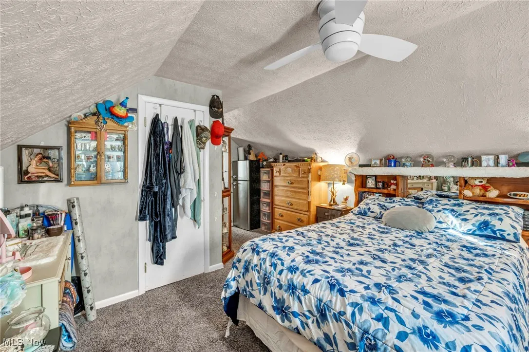 Carpeted bedroom with vaulted ceiling, freestanding refrigerator, a textured ceiling, ceiling fan, and a closet