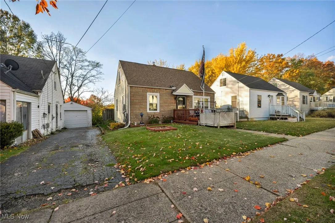 View of front of home with a deck, a front lawn, stone siding, an outbuilding, and a garage