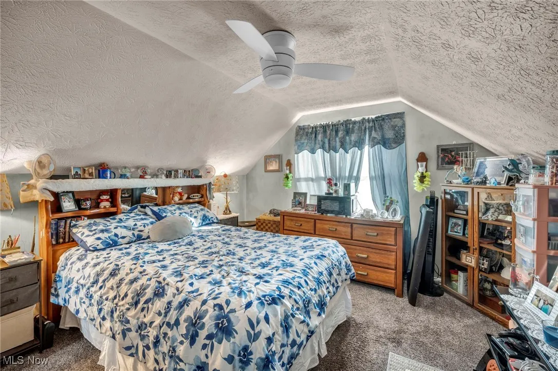 Carpeted bedroom featuring a textured ceiling, vaulted ceiling, and ceiling fan