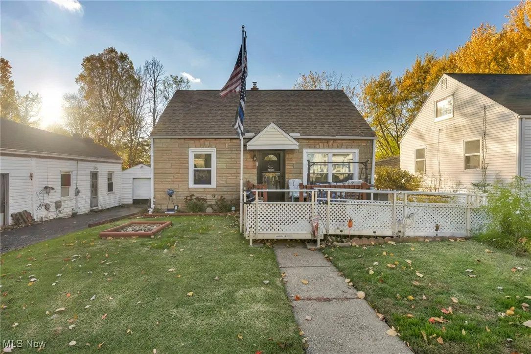 View of front of property with stone siding, roof with shingles, a front yard, and a garden