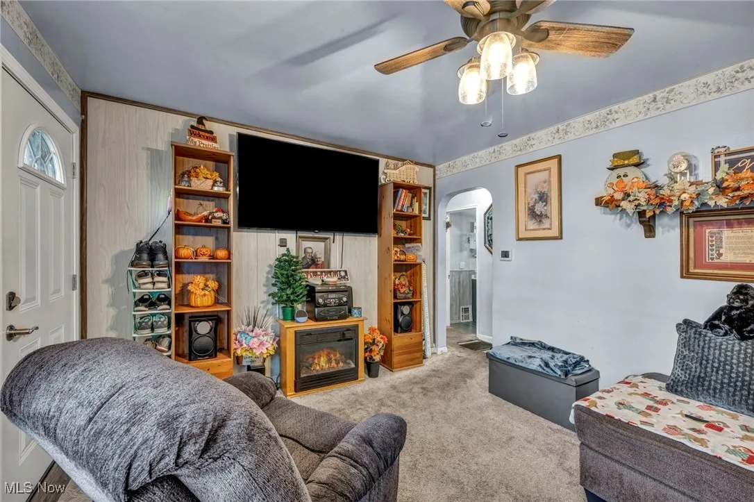 Carpeted living area featuring arched walkways and ceiling fan