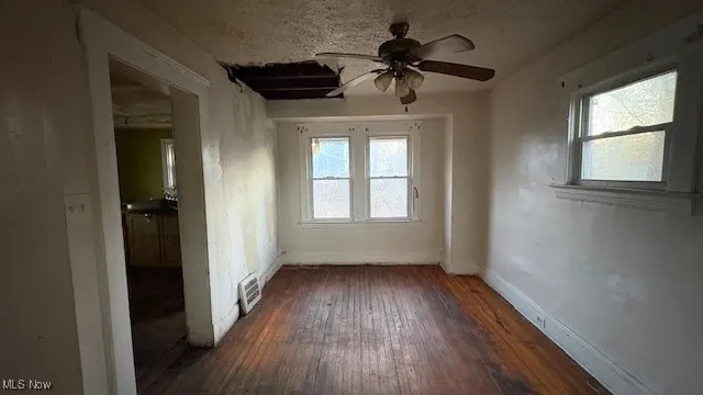Empty room featuring a ceiling fan, dark wood finished floors, plenty of natural light, and a textured ceiling