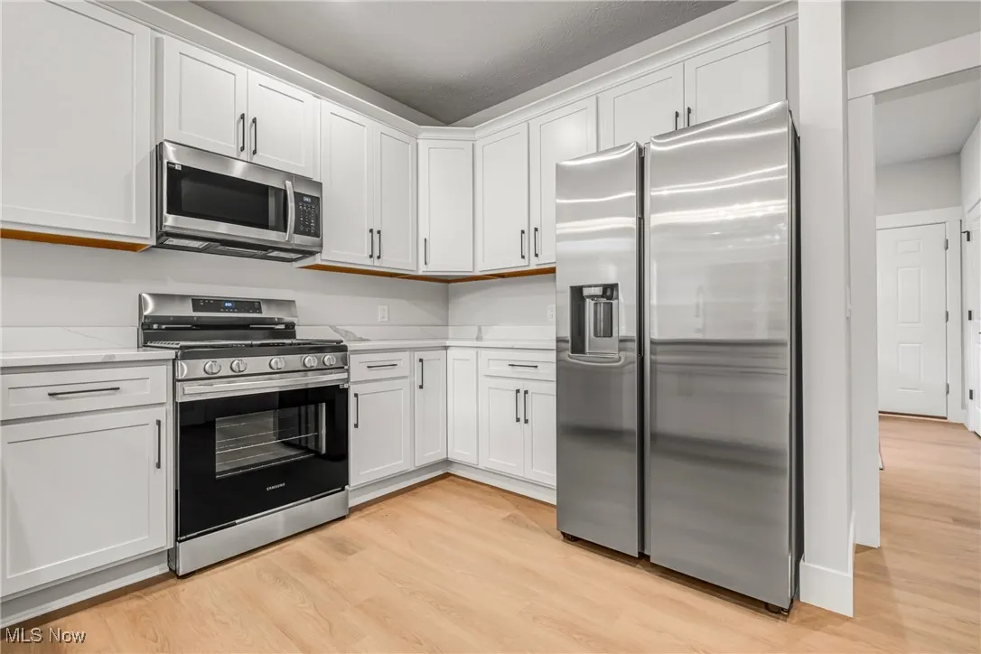 Kitchen featuring light stone counters, light hardwood / wood-style flooring, white cabinets, and appliances with stainless steel finishes