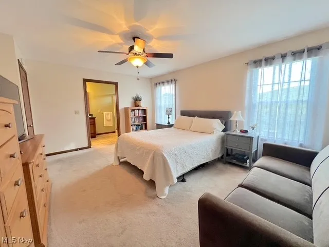 Bedroom with ensuite bath, light carpet, and a ceiling fan