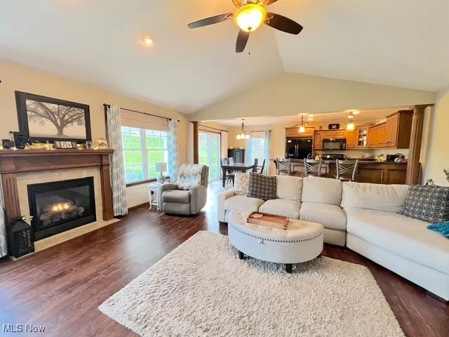 Living room featuring a fireplace with flush hearth, dark wood finished floors, vaulted ceiling, and ceiling fan