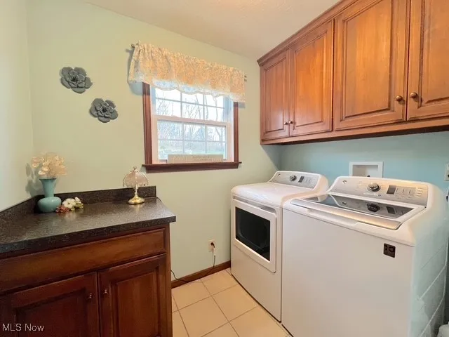 Washroom with cabinet space, light tile patterned floors, washing machine and dryer, and a textured ceiling