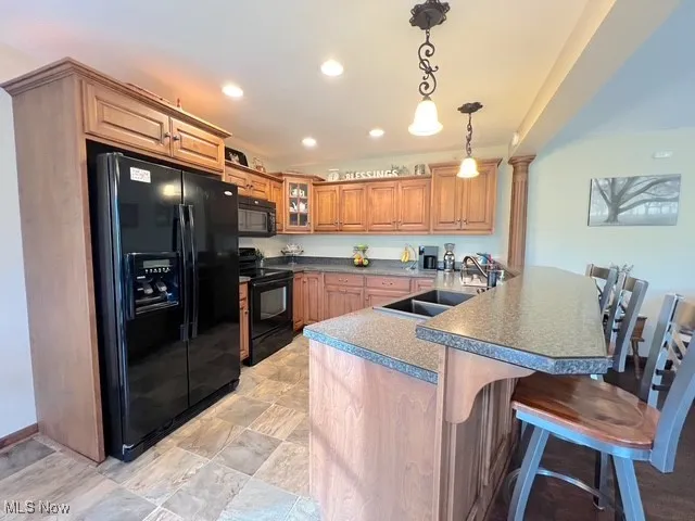 Kitchen with black appliances, a breakfast bar area, a peninsula, brown cabinetry, and decorative light fixtures