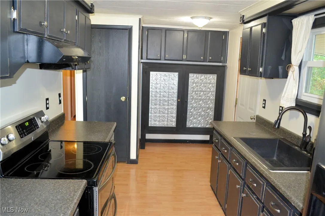 Kitchen featuring dark countertops, stainless steel electric range oven, light wood-type flooring, and under cabinet range hood