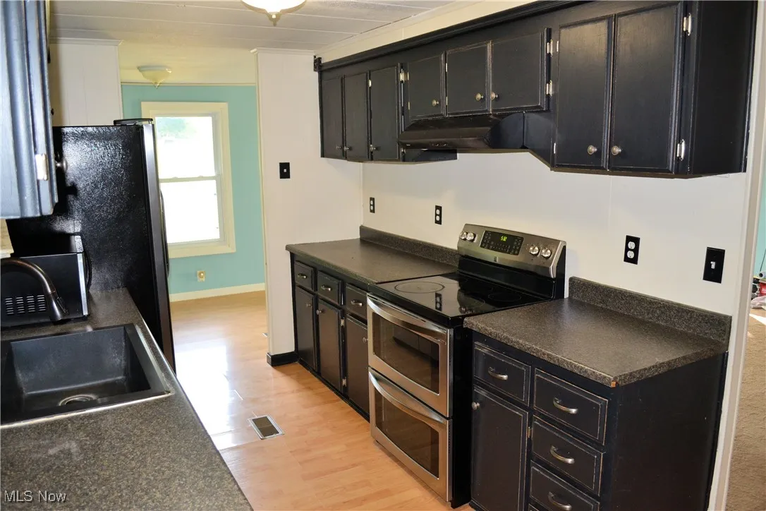 Kitchen featuring range with two ovens, dark countertops, dark cabinets, light wood-style flooring, and extractor fan