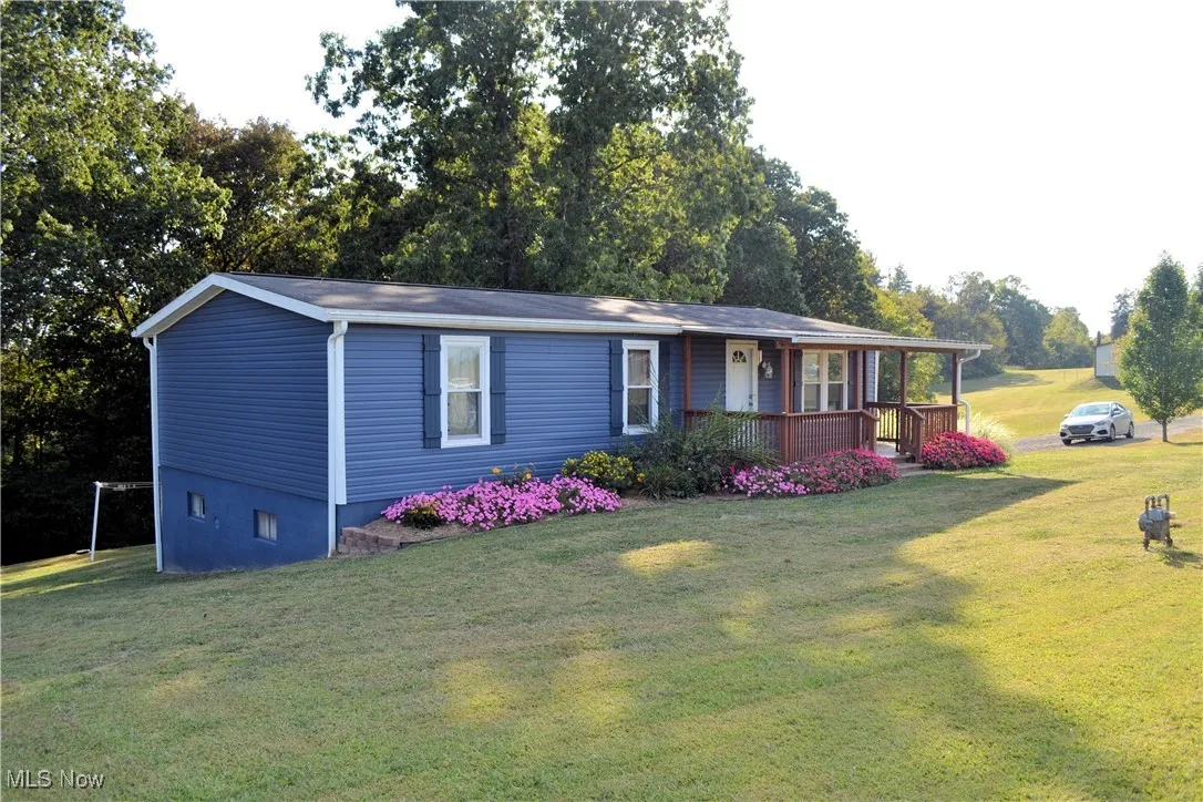 View of front of property featuring a front lawn, covered porch, and view of wooded area
