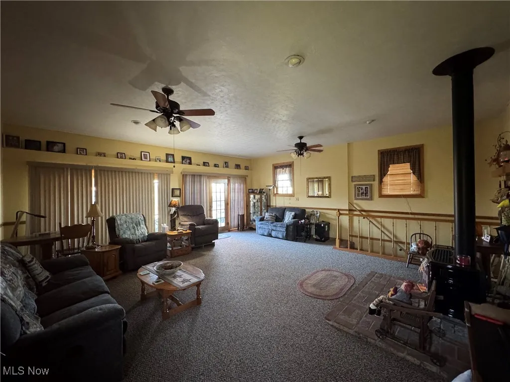 Living area featuring a wood stove, carpet floors, and a ceiling fan