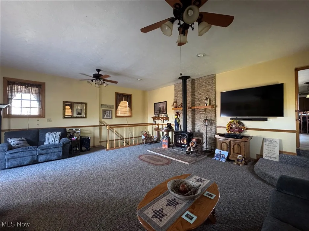 Living area featuring a wood stove, ceiling fan, and carpet