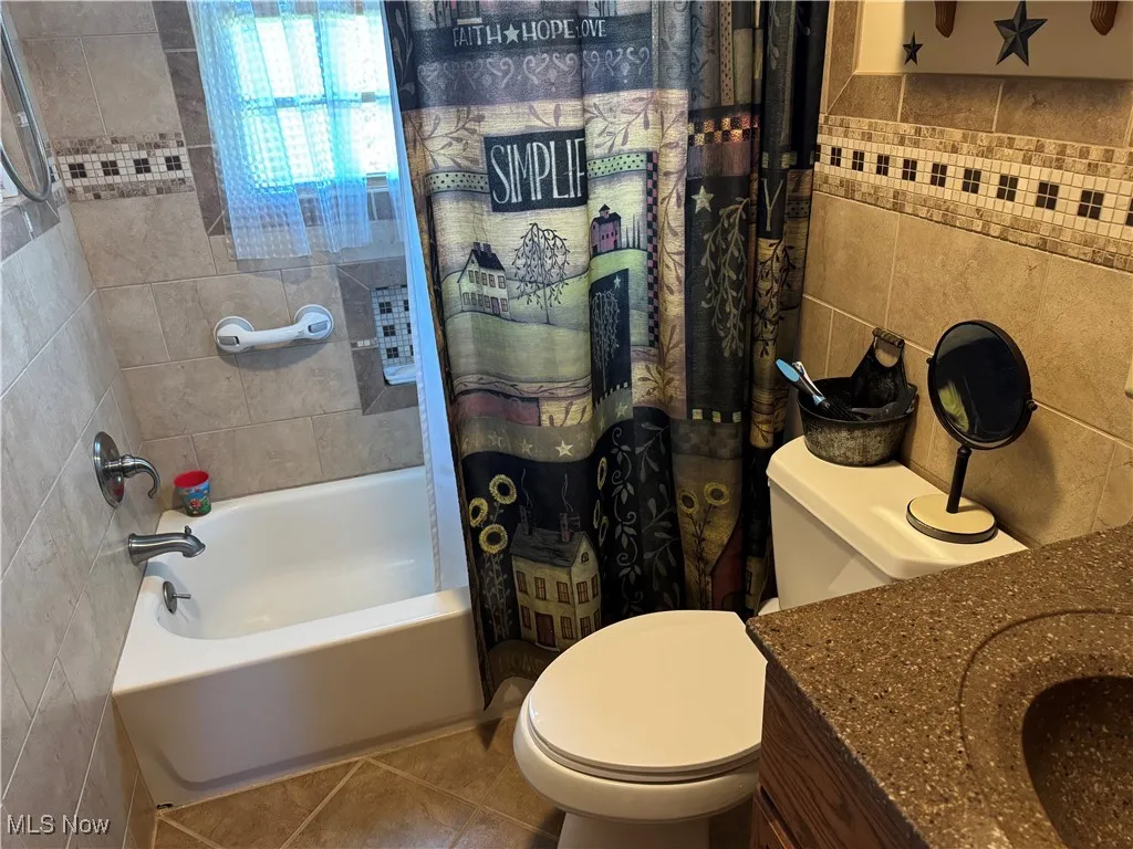 Bathroom with tile walls, tile patterned floors, vanity, and shower / bath combo with shower curtain