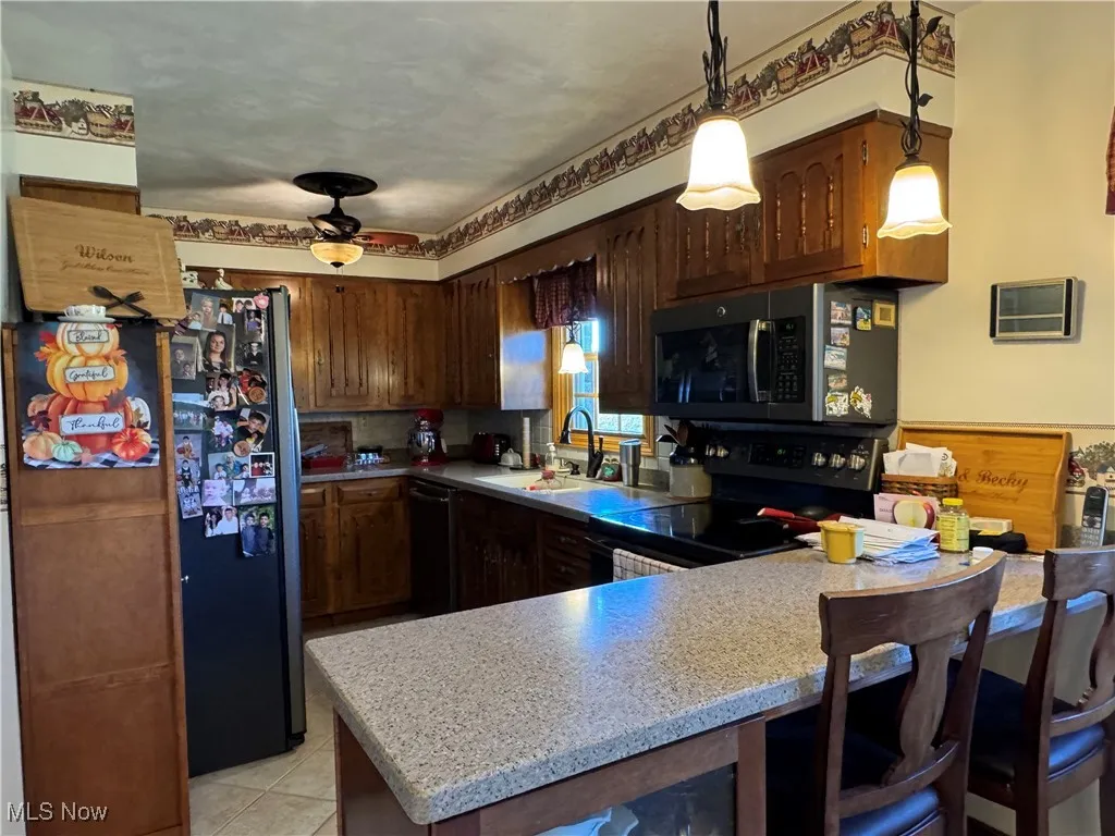 Kitchen featuring black appliances, a peninsula, light countertops, pendant lighting, and light tile patterned floors