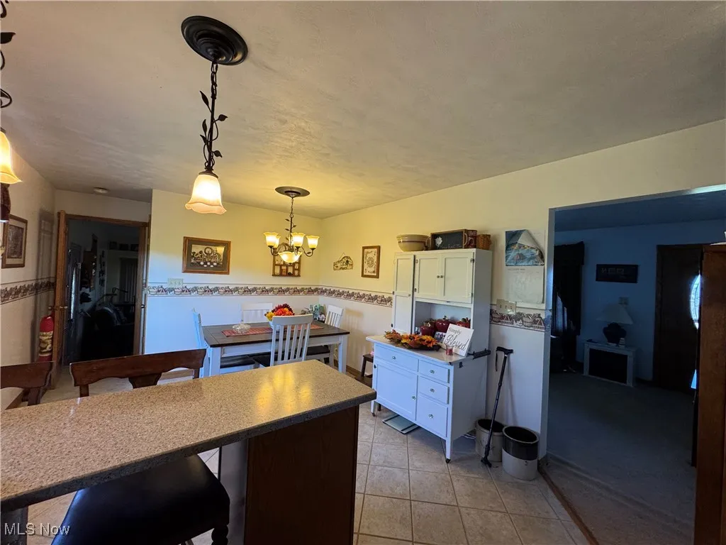 Kitchen featuring a kitchen breakfast bar, decorative light fixtures, light tile patterned flooring, white cabinetry, and a chandelier
