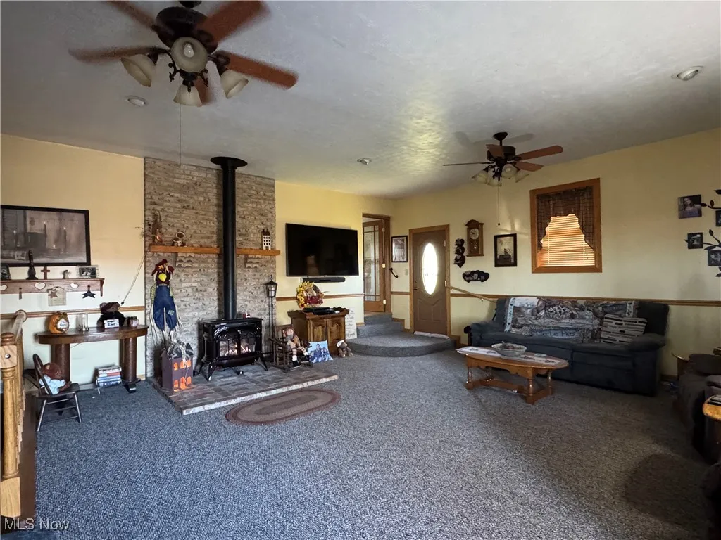 Living room with a wood stove, a ceiling fan, and carpet flooring