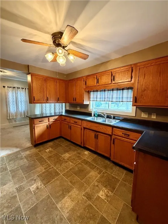 Kitchen featuring dark countertops, brown cabinetry, stone tile flooring, and a ceiling fan