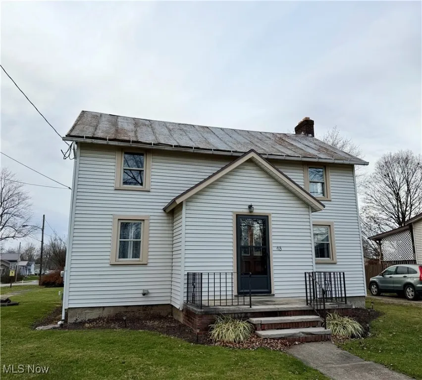 View of front of home with a front lawn, a chimney, and a standing seam roof
