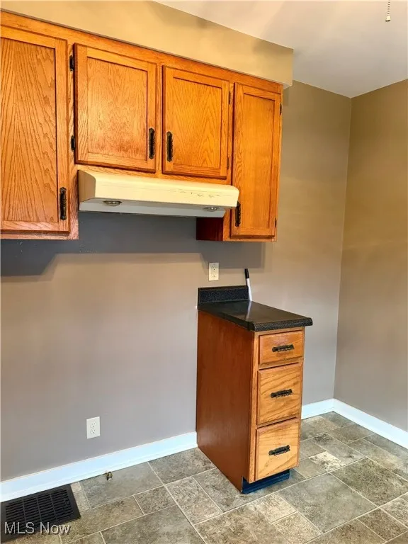 Kitchen featuring dark countertops, brown cabinets, stone tile floors, and under cabinet range hood