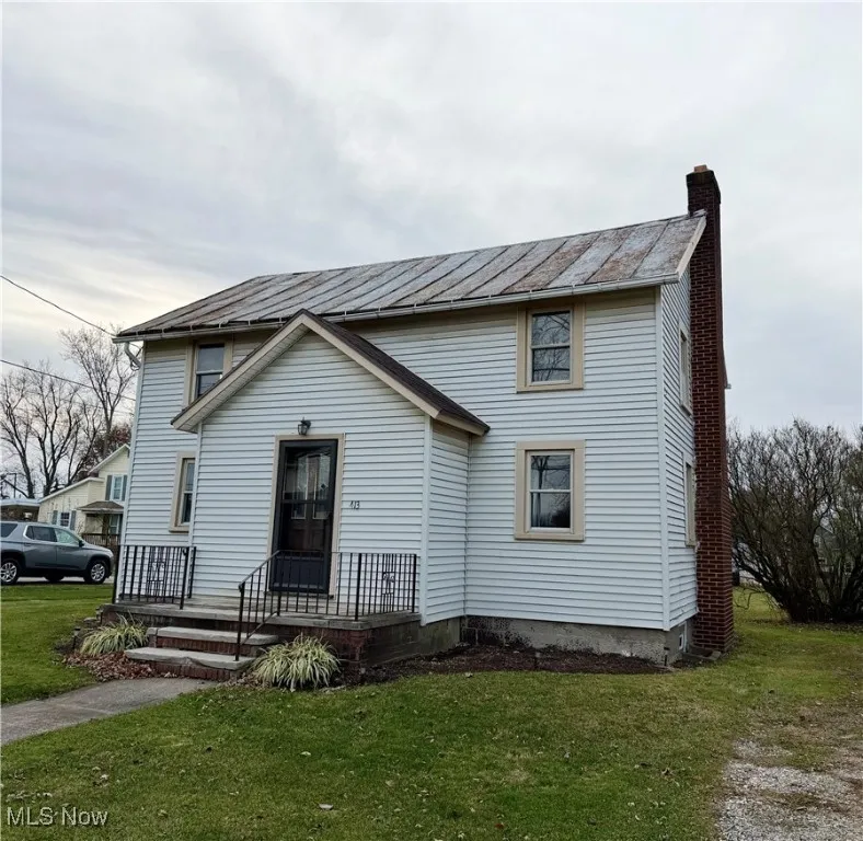 View of front of home featuring a chimney, a standing seam roof, a front lawn, and a metal roof