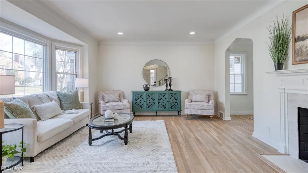 Living area with arched walkways, wood finished floors, a tile fireplace, recessed lighting, and crown molding