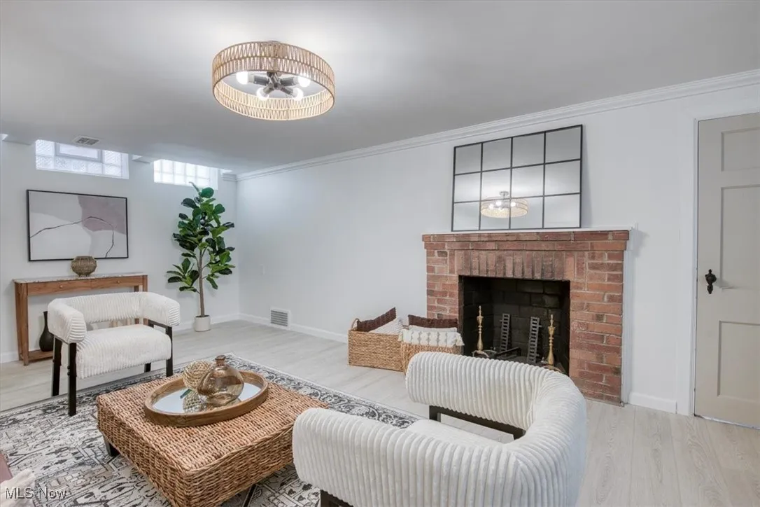 Living room featuring a brick fireplace, wood finished floors, and ornamental molding