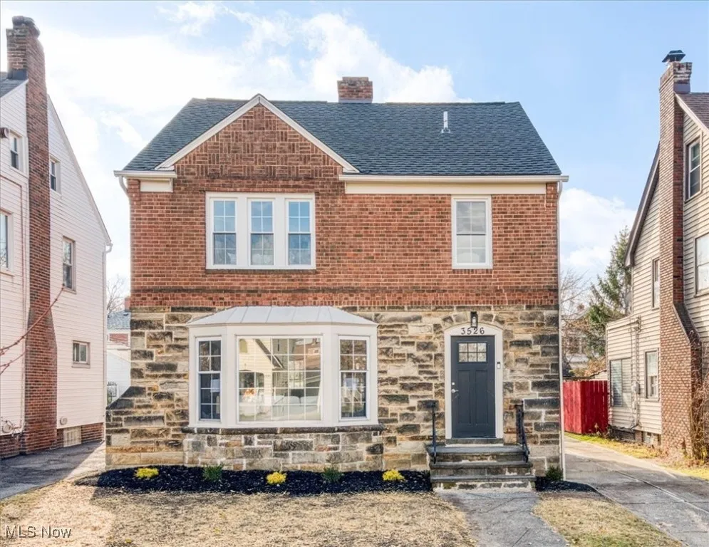 View of front facade with stone siding, a shingled roof, and a chimney