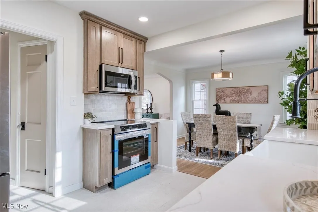 Kitchen with stainless steel appliances, pendant lighting, light stone countertops, decorative backsplash, and arched walkways