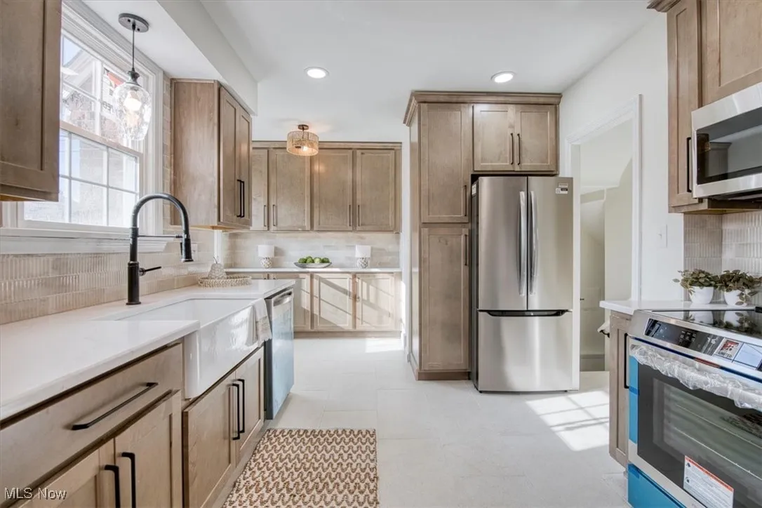 Kitchen featuring stainless steel appliances, tasteful backsplash, decorative light fixtures, light stone countertops, and recessed lighting