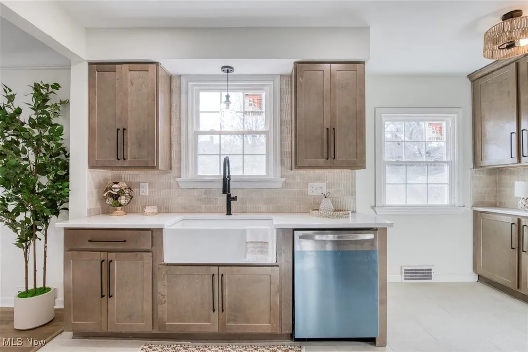 Kitchen with stainless steel dishwasher, tasteful backsplash, hanging light fixtures, light stone countertops, and brown cabinetry