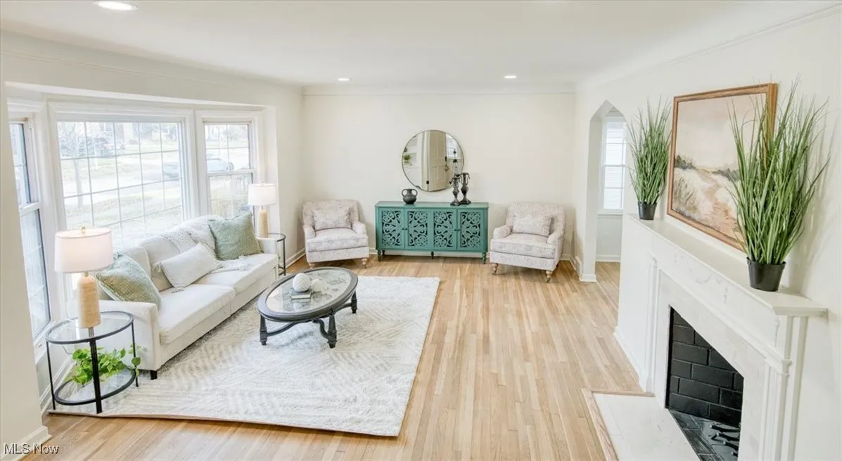 Living room featuring light wood-style floors, healthy amount of natural light, a fireplace with flush hearth, recessed lighting, and arched walkways