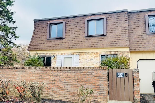 View of property with mansard roof, roof with shingles, a gate, and brick siding
