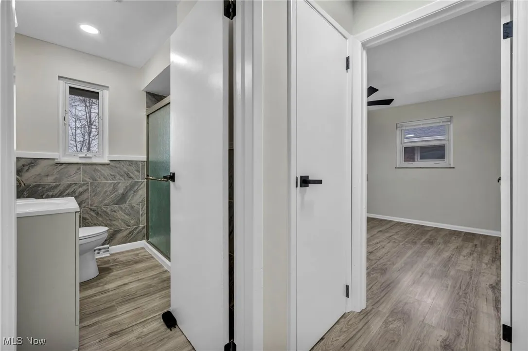 Full bath featuring tile walls, a stall shower, vanity, a wainscoted wall, and light wood finished floors