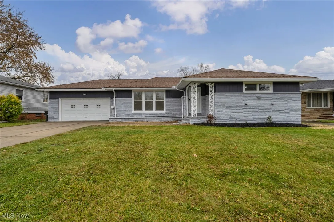 Ranch-style home featuring stone siding, concrete driveway, a front yard, and a garage