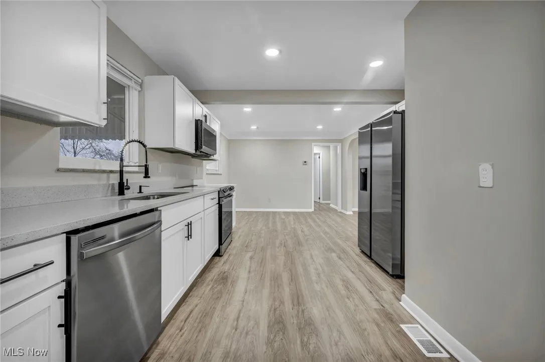 Kitchen featuring appliances with stainless steel finishes, white cabinetry, light stone countertops, recessed lighting, and light wood-style floors