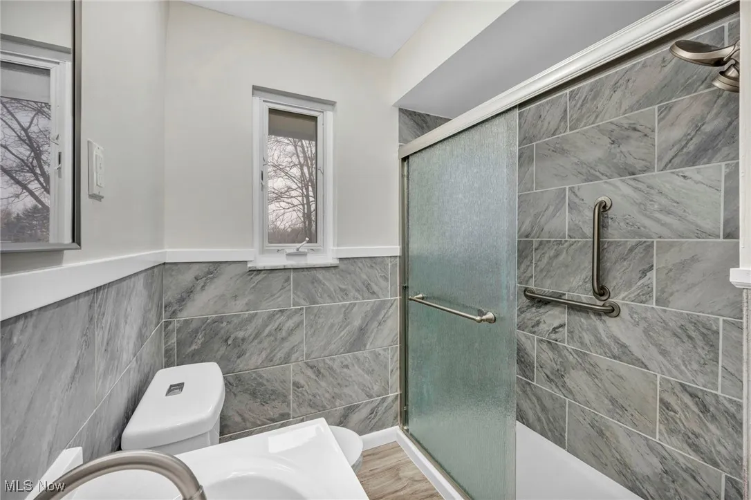 Bathroom with a stall shower, tile walls, and a wainscoted wall