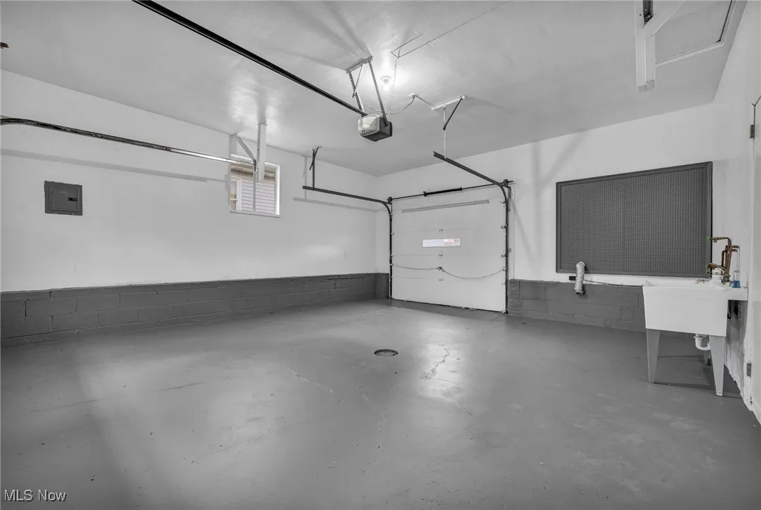 Garage featuring concrete block wall, electric panel, and a garage door opener