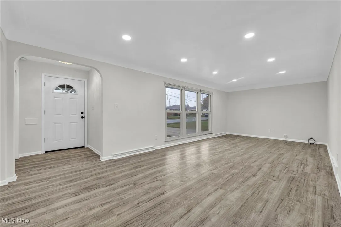 living room with light wood-type flooring, recessed lighting, baseboard heating, and arched walkways