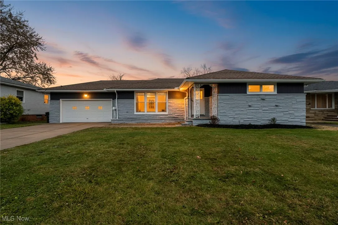 View of front of house with a front lawn, stone siding, driveway, and a garage