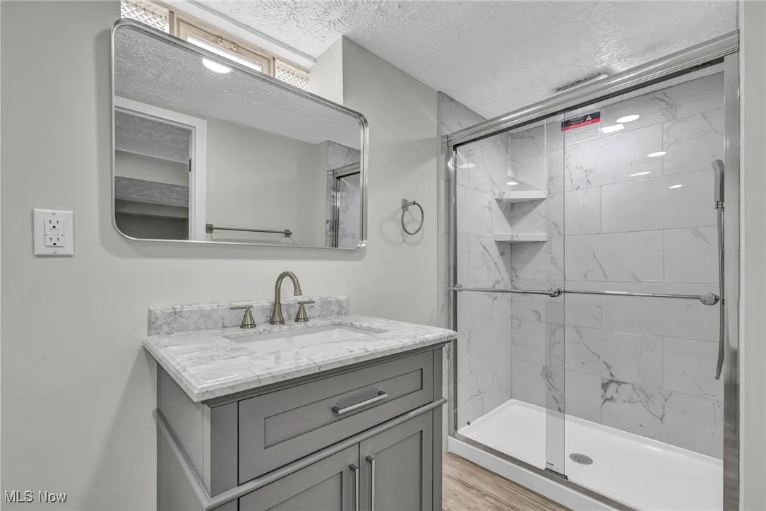 Bathroom featuring a textured ceiling, vanity, and a marble finish shower
