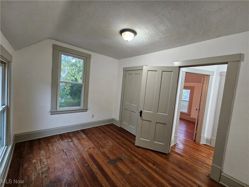 Unfurnished bedroom with a textured ceiling, multiple windows, dark wood-type flooring, a closet, and vaulted ceiling