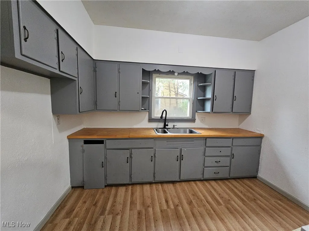 Kitchen featuring gray cabinetry, open shelves, light wood-type flooring, a textured wall, and wooden counters