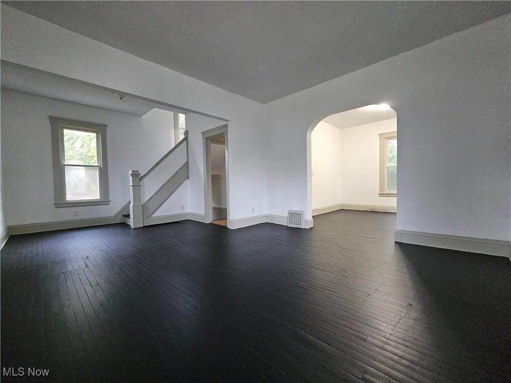 Unfurnished living room featuring arched walkways, dark wood finished floors, and stairway