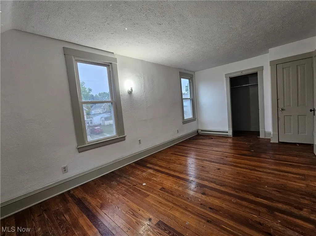 Unfurnished bedroom featuring a textured ceiling, a textured wall, dark wood finished floors, a closet, and baseboard heating