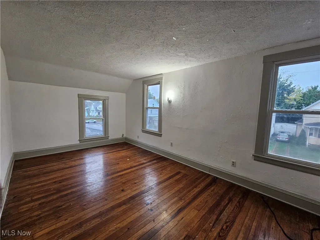 Unfurnished room featuring a textured ceiling, a textured wall, dark wood-style floors, and lofted ceiling