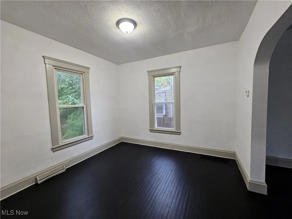 Empty room featuring arched walkways, a textured ceiling, and wood-type flooring